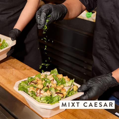 sprinkling savory herbs on MIXT Caesar salad